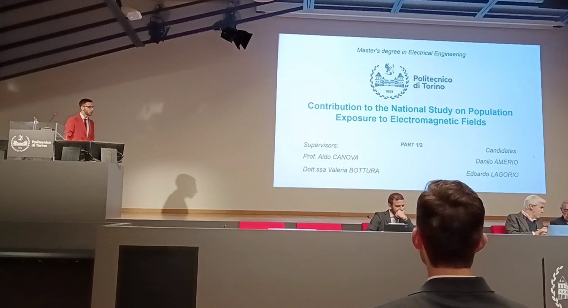 Edoardo Lagorio che inizia la discussione di tesi sullo scranno, mentre la stessa è proiettata sul muro a favore del pubblico. Di schiena il collega Danilo Amerio