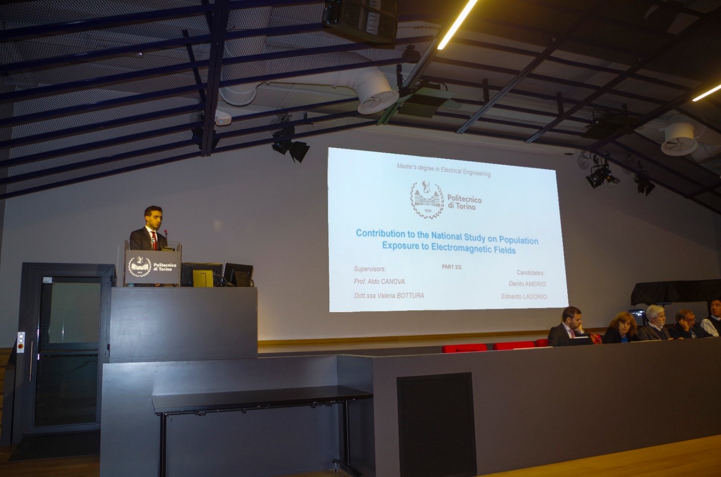 Danilo Amerio che inizia la discussione di tesi sullo scranno, mentre la stessa è proiettata sul muro a favore del pubblico.