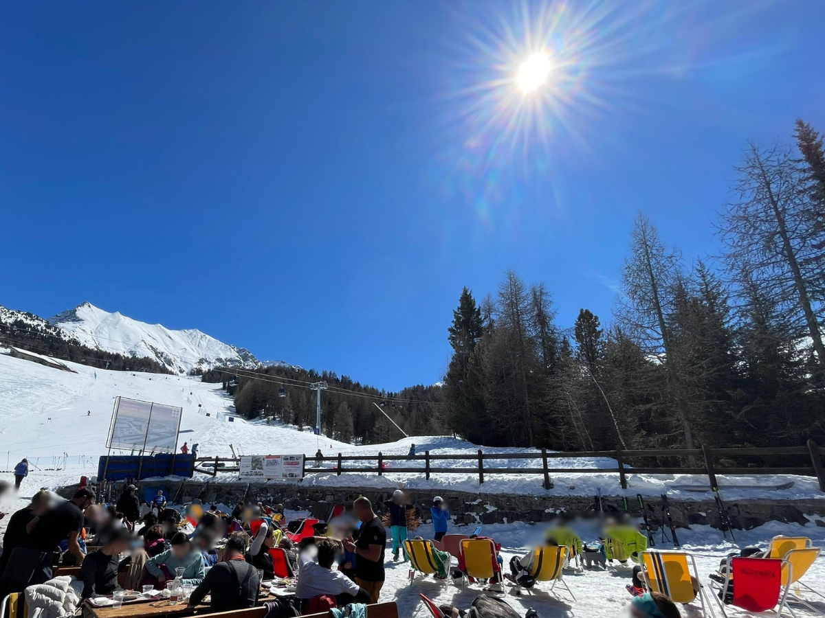 persone che prendono il sole nel dehor di un locale situato sulle piste da sci di Pila , alberi, cielo azzurro e sole
