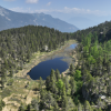 immagine aerea dalla quale si vedono alberi, lago, zona umida circostante, montagne e nuvole e cielo sullo sfondo