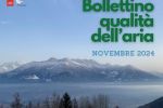 alberi in primo piano, strato di polveri, montagna in secondo piano. Titolo Bollettino qualità dell'aria novembre 2024