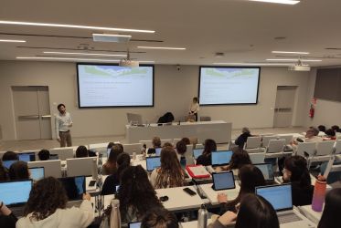 studenti e studentesse riprese di schiena sedute in un'aultauniversitaria mentre seguono il workshop sui servizi ecosistemici. Nicola Favretto e Marta Galvagno presiedono