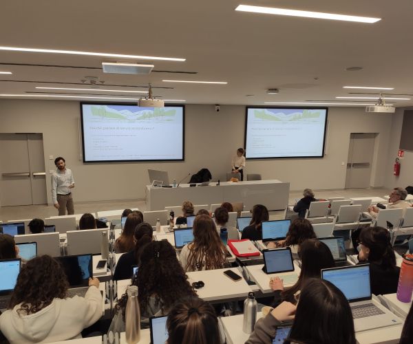 studenti e studentesse riprese di schiena sedute in un'aultauniversitaria mentre seguono il workshop sui servizi ecosistemici. Nicola Favretto e Marta Galvagno presiedono