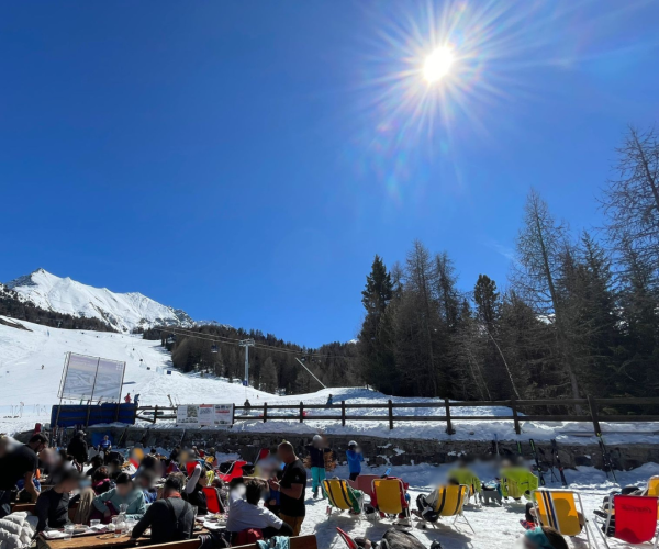 persone che prendono il sole nel dehor di un locale situato sulle piste da sci di Pila , alberi, cielo azzurro e sole