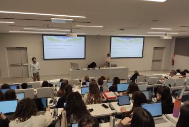 studenti e studentesse riprese di schiena sedute in un'aultauniversitaria mentre seguono il workshop sui servizi ecosistemici. Nicola Favretto e Marta Galvagno presiedono