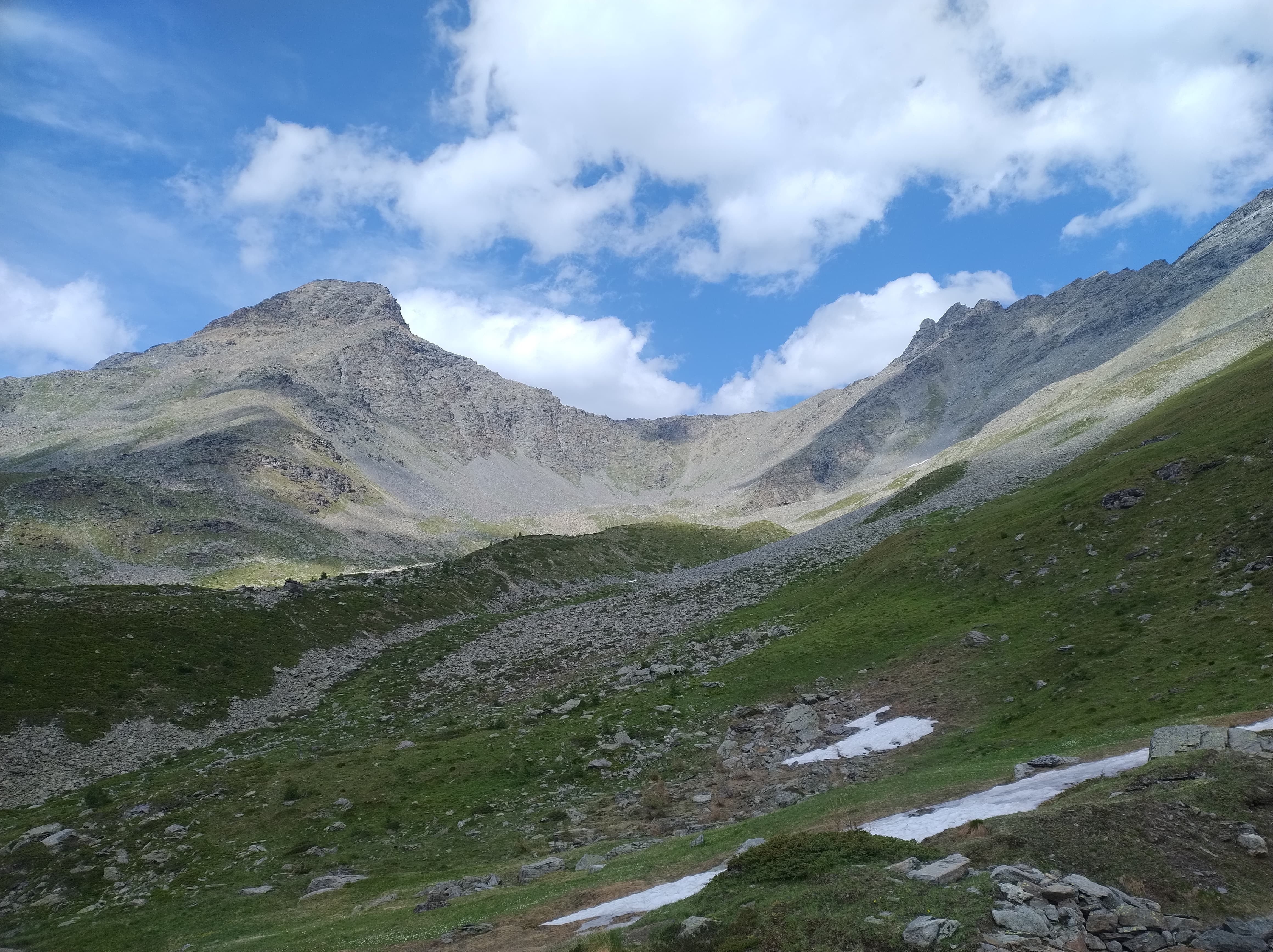 Vallone di Sort - del Parco Nazionale del Gran Paradiso, in Comune di Rhêmes-Notre-Dame. Erba in primo piano e chiazze di neve, territorio montano, pendenza, montagne in secondo piano, nuvole in cielo